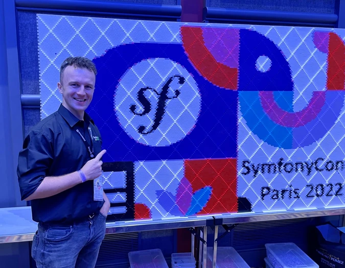 Mężczyzna pozujący obok ściany z grafiką pixel art SymfonyCon Paris 2022