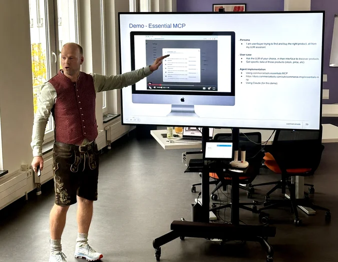 Mężczyzna w tradycyjnych bawarskich spodniach lederhosen prowadzący prezentację na temat „Essential MCP” przy użyciu dużego ekranu