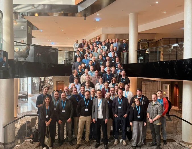 Duża grupa członków zespołu pozuje do zdjęcia grupowego na szerokich schodach w nowoczesnym foyer