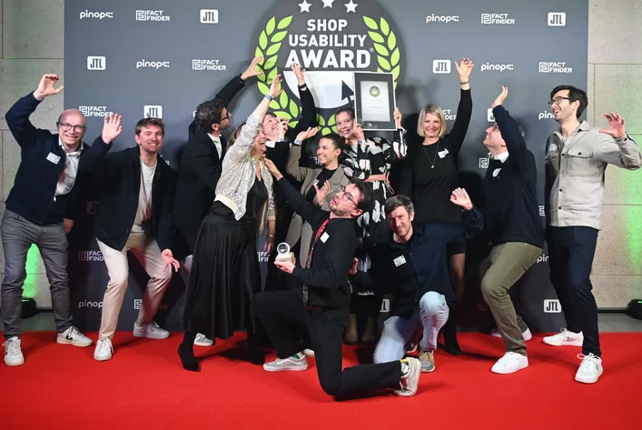 A group of people celebrating on a red carpet with an award, under a "Shop Usability Award" banner.