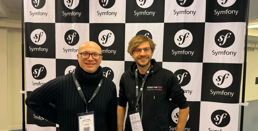 Dwóch mężczyzn pozuje na tle czarno-białej szachownicy z logo Symfony