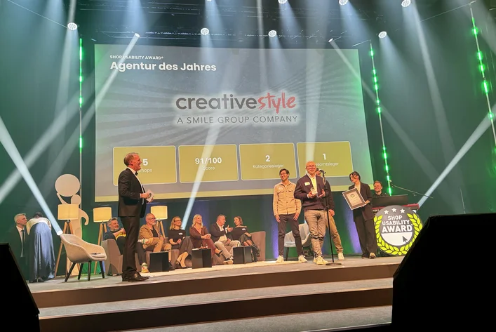 People on stage receiving an award for "Agentur des Jahres" from SCD; the background displays scores and achievements.