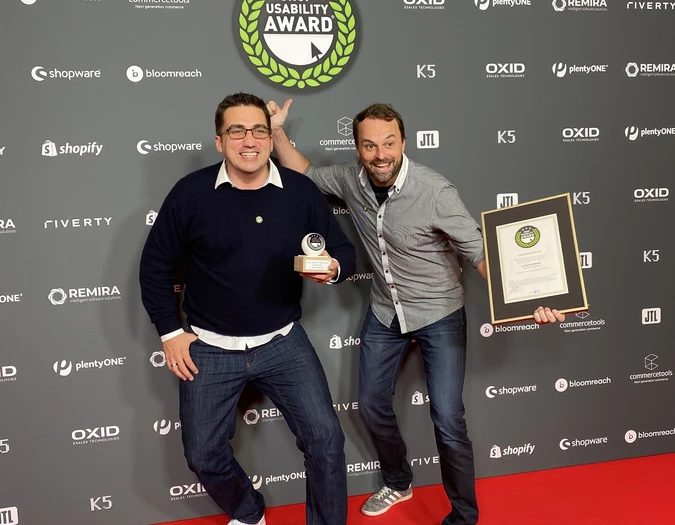 Dwóch mężczyzn pozuje na czerwonym dywanie z trofeum i certyfikatem Shop Usability Award