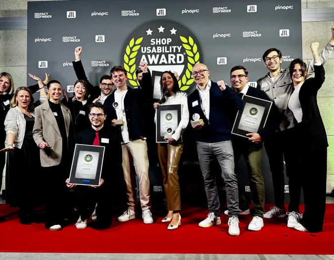 A group of people celebrating on a red carpet, holding awards in front of a "Shop Usability Award" backdrop.