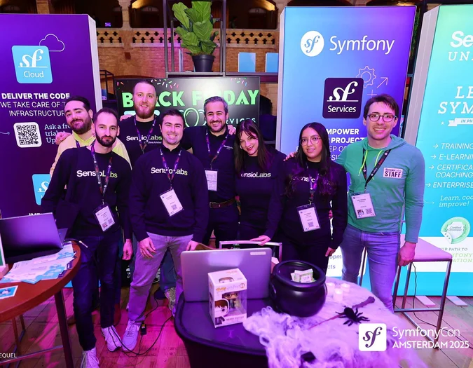Grupa osób na stoisku SymfonyCon Amsterdam 2025 z różnymi banerami firmowymi